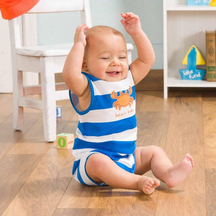 Baby sitting on a wooden floor wearing a blue and white striped outfit with a crab design.