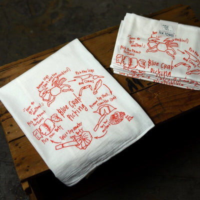 White tea towels with red graphics and text on a wooden surface