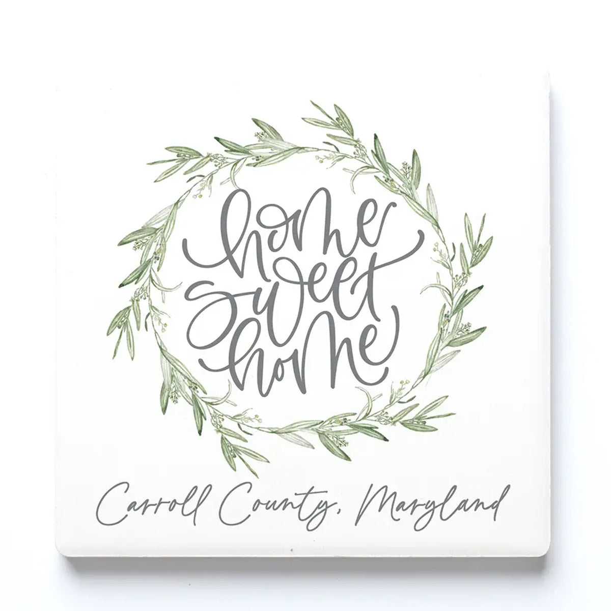 A square ceramic drink coaster with a green leaf wreath and gray script reading “home sweet home,” with “Carroll County, Maryland” written below in gray script.