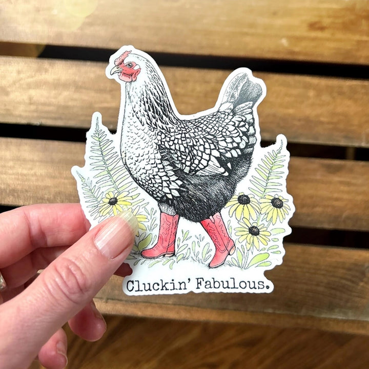 A die-cut sticker featuring a black and white illustrated chicken wearing red cowboy boots, surrounded by yellow flowers and green leaves, with the text &