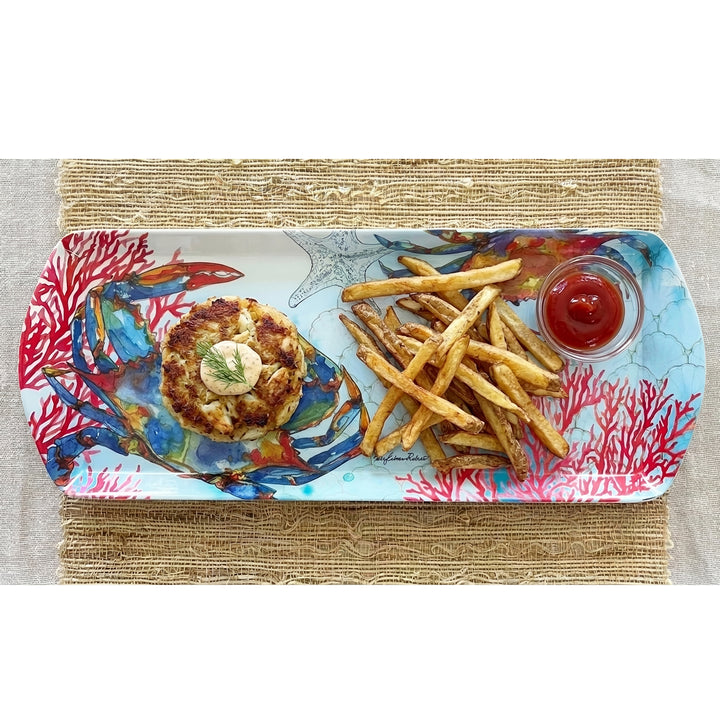 A rectangular bamboo serving platter with a colorful crab and ocean-themed print, featuring a crab cake, fries, and a small cup of ketchup, placed on a woven placemat.