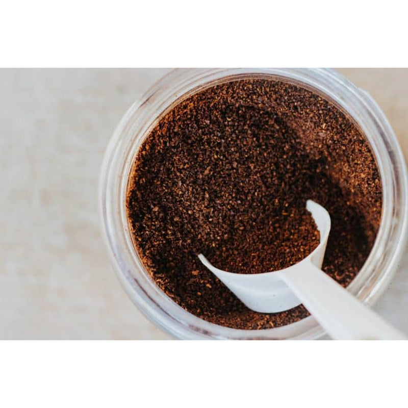 Jar of coffee grounds with a white spoon on a light background