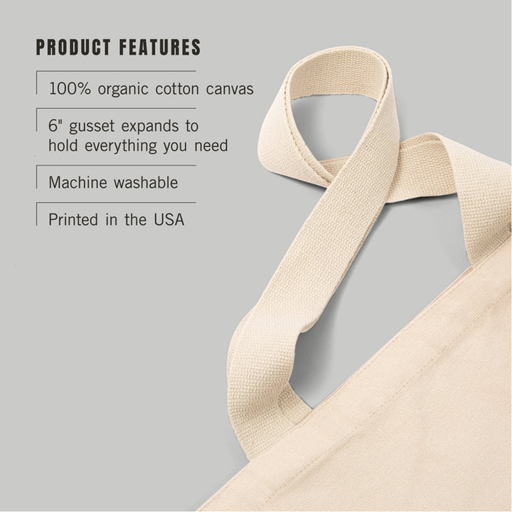 A close-up of a beige canvas tote bag strap on a light gray background with text listing product features: 100% organic cotton canvas, 6" gusset that expands, machine washable, and printed in the USA.