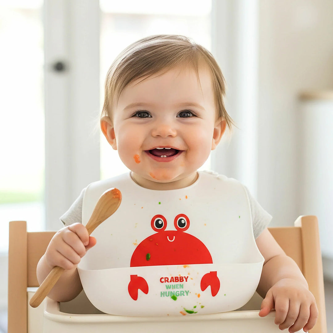 Child wearing a bib with a crab design, sitting in a high chair.