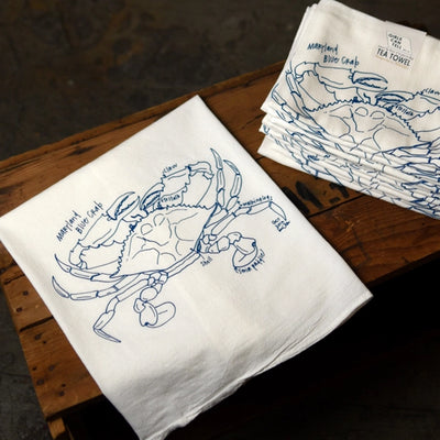 White tea towels with blue crab illustrations on a wooden surface