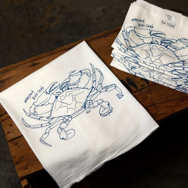 White tea towels with blue crab illustrations on a wooden surface