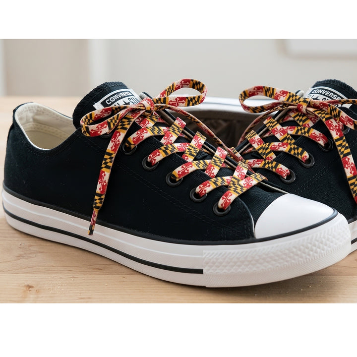 Black canvas low-top sneakers with white rubber toe caps and soles, featuring Maryland flag shoelaces.