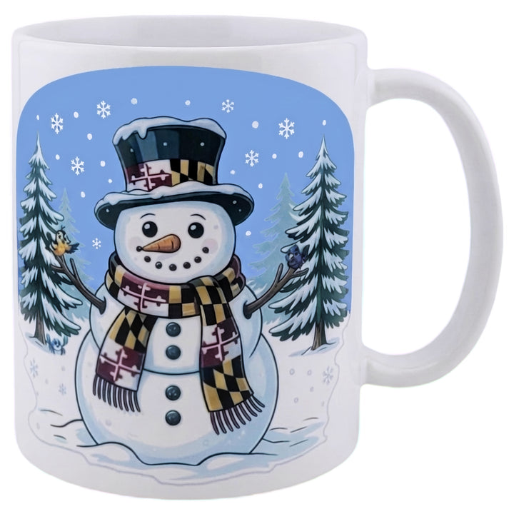 Maryland snowman coffee mug - a snowman with a Maryland flag scarf and hat with an oriole and a raven perched on the wood branch arms with pine trees in the background all on a white coffee mug