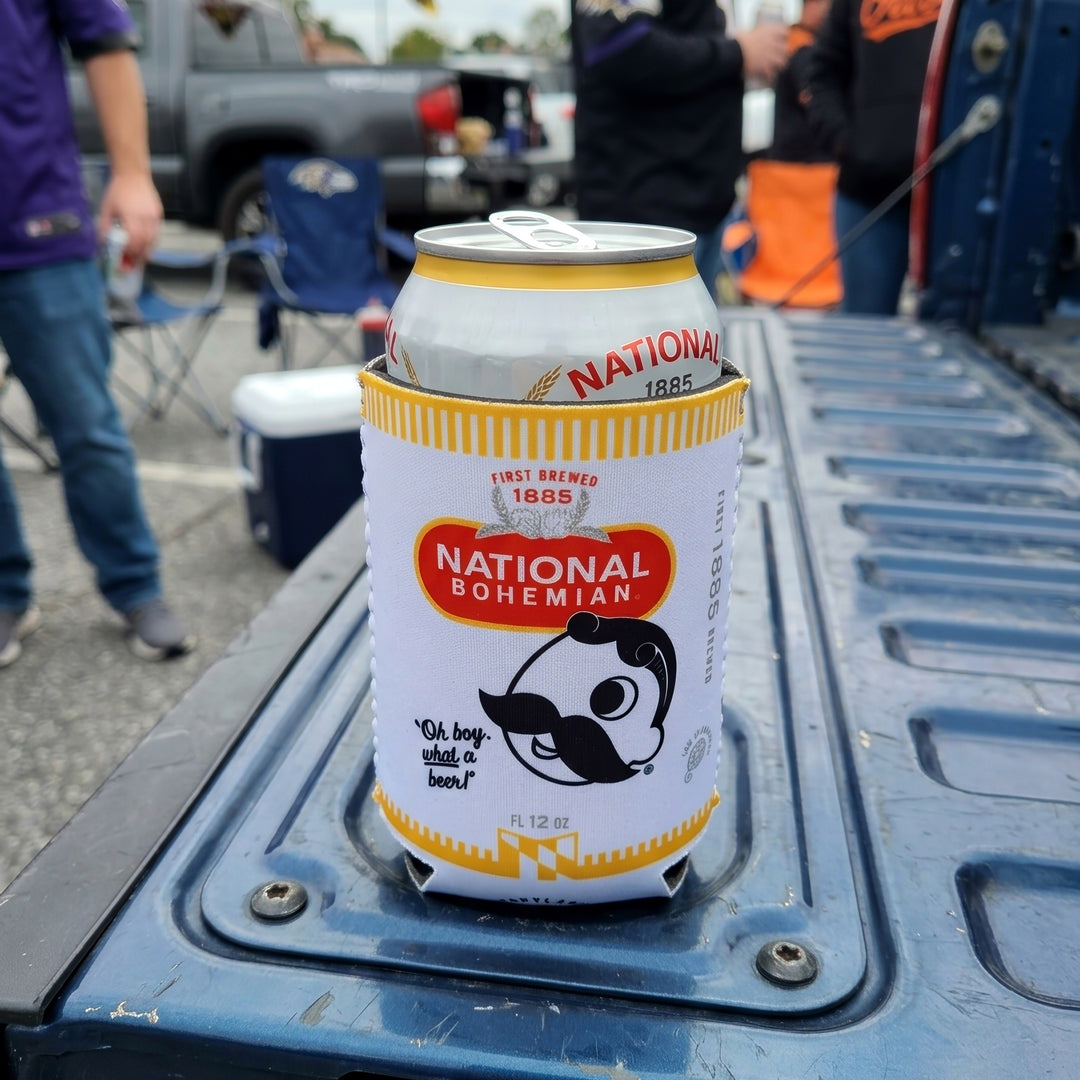 A Natty Boh Can Coolie sitting on the tailgate of a blue pickup truck at an outdoor event.