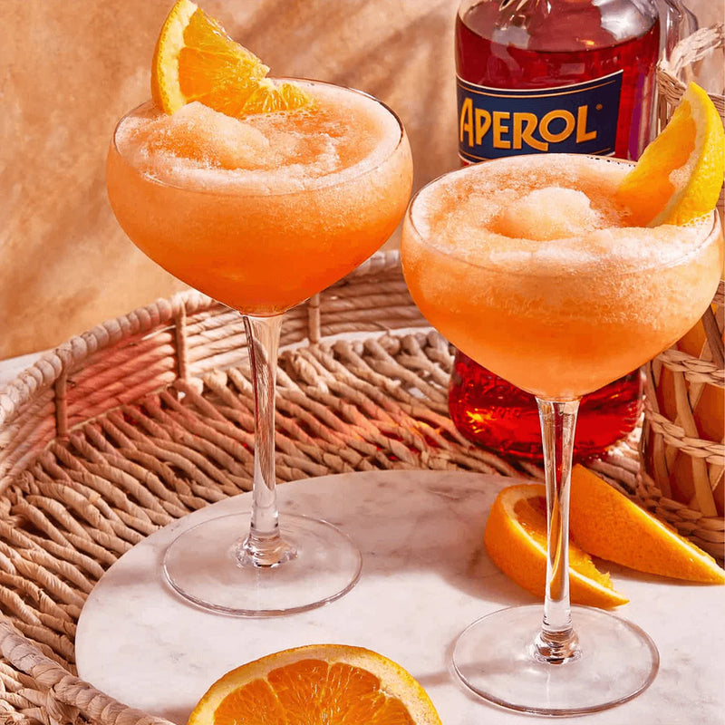 Two orange cocktails with Aperol bottle and oranges on a woven tray