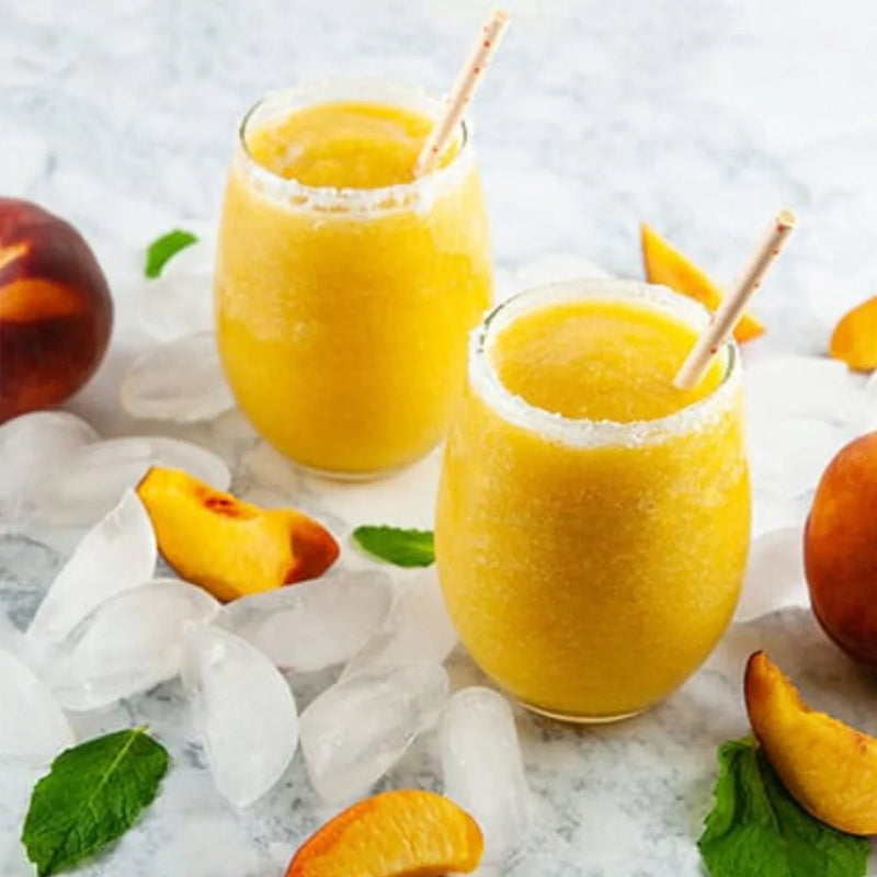 Two glasses of peach bellini frozen cocktails with ice and peaches on a light background