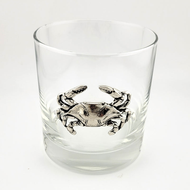 A clear glass rocks tumbler featuring a detailed pewter crab motif at the center, set against a plain white background.