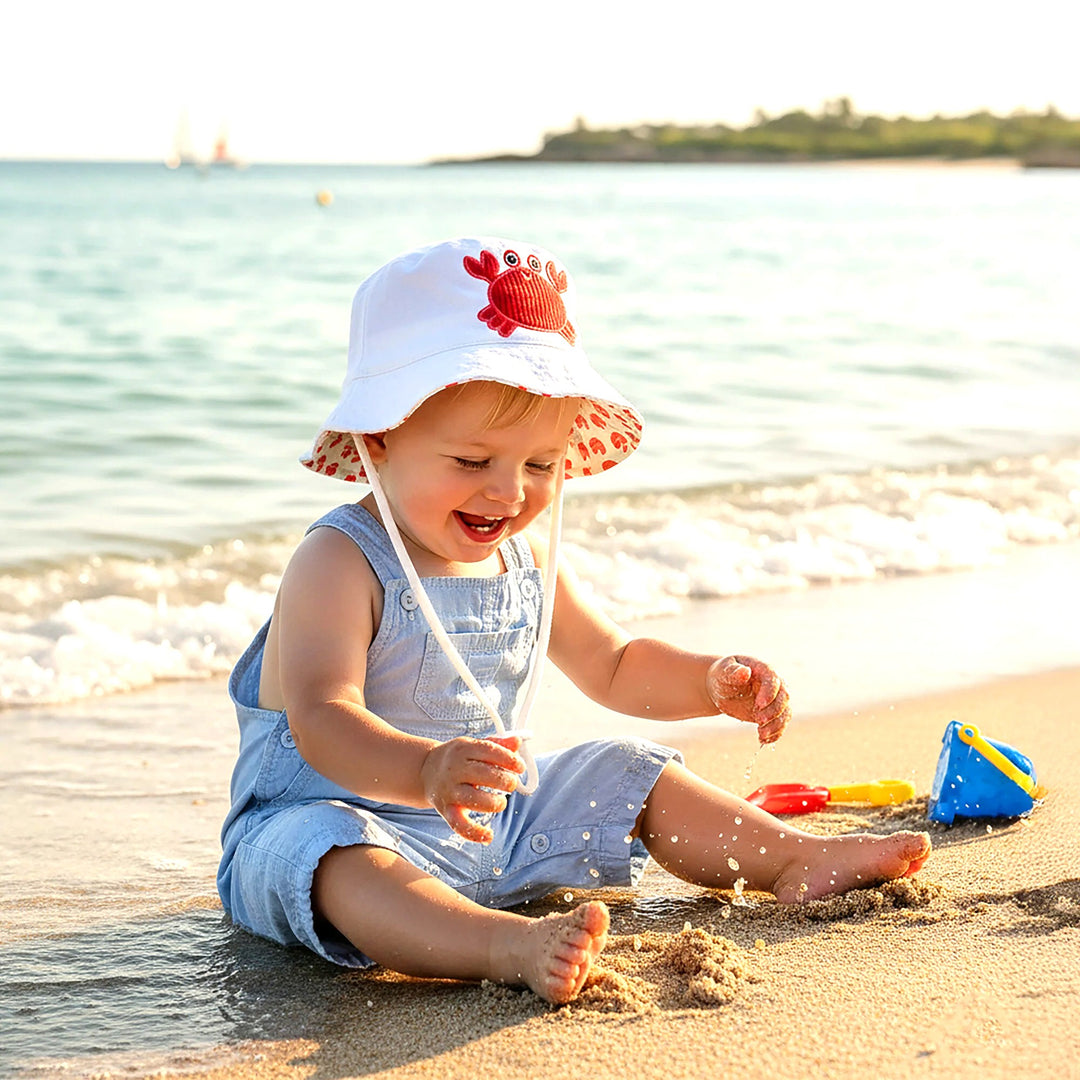 Child playing on a beach wearing a sun hat with a crab design