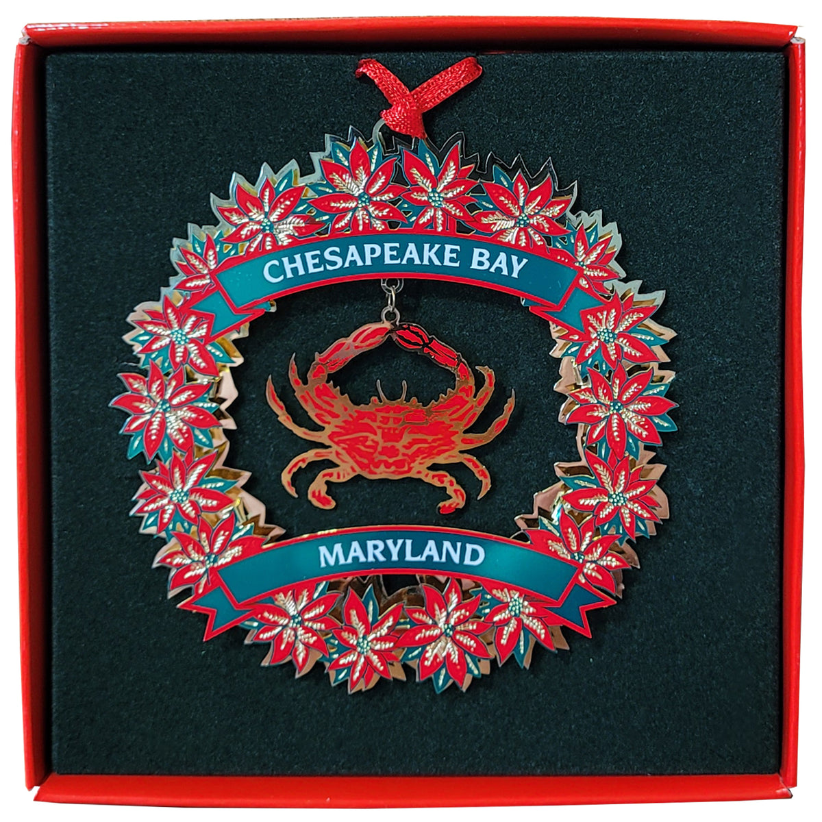A Christmas ornament shaped like a wreath with a red crab in the center, blue banners reading 'CHESAPEAKE BAY' and 'MARYLAND,' and red-and-white floral cutouts around the border, displayed inside a red gift box.