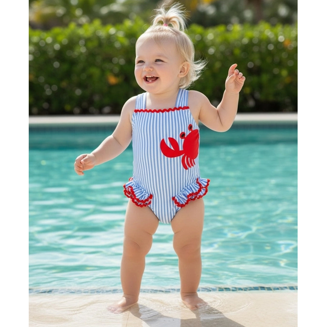 Child in a red, white, and blue swimsuit with a crab design by a pool.