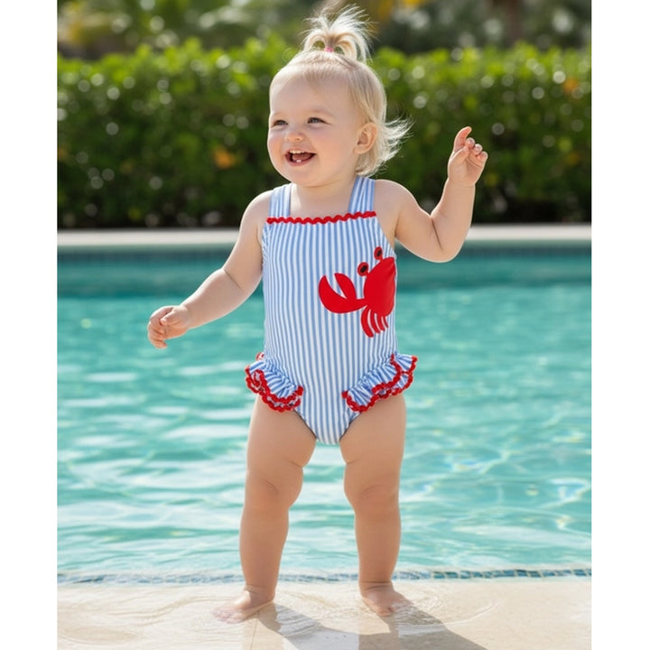 Child in a red, white, and blue swimsuit with a crab design by a pool.