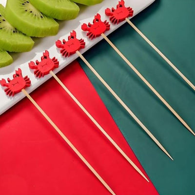Red crab-shaped skewers on a white tray with sliced kiwis on a red and green background