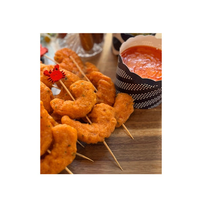 Crab skewers of shrimp on a wooden board next to a bowl of cocktail sauce.