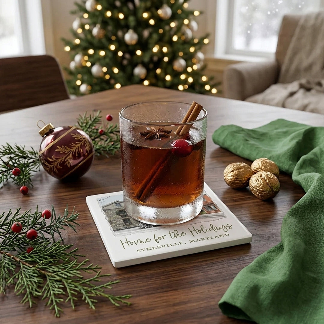 Square ceramic drink coaster featuring a winter street scene in Sykesville, Maryland, with a snow-covered Christmas tree in front of historic buildings.