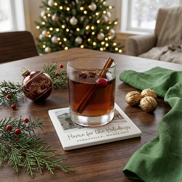 Square ceramic drink coaster featuring a winter street scene in Sykesville, Maryland, with a snow-covered Christmas tree in front of historic buildings.