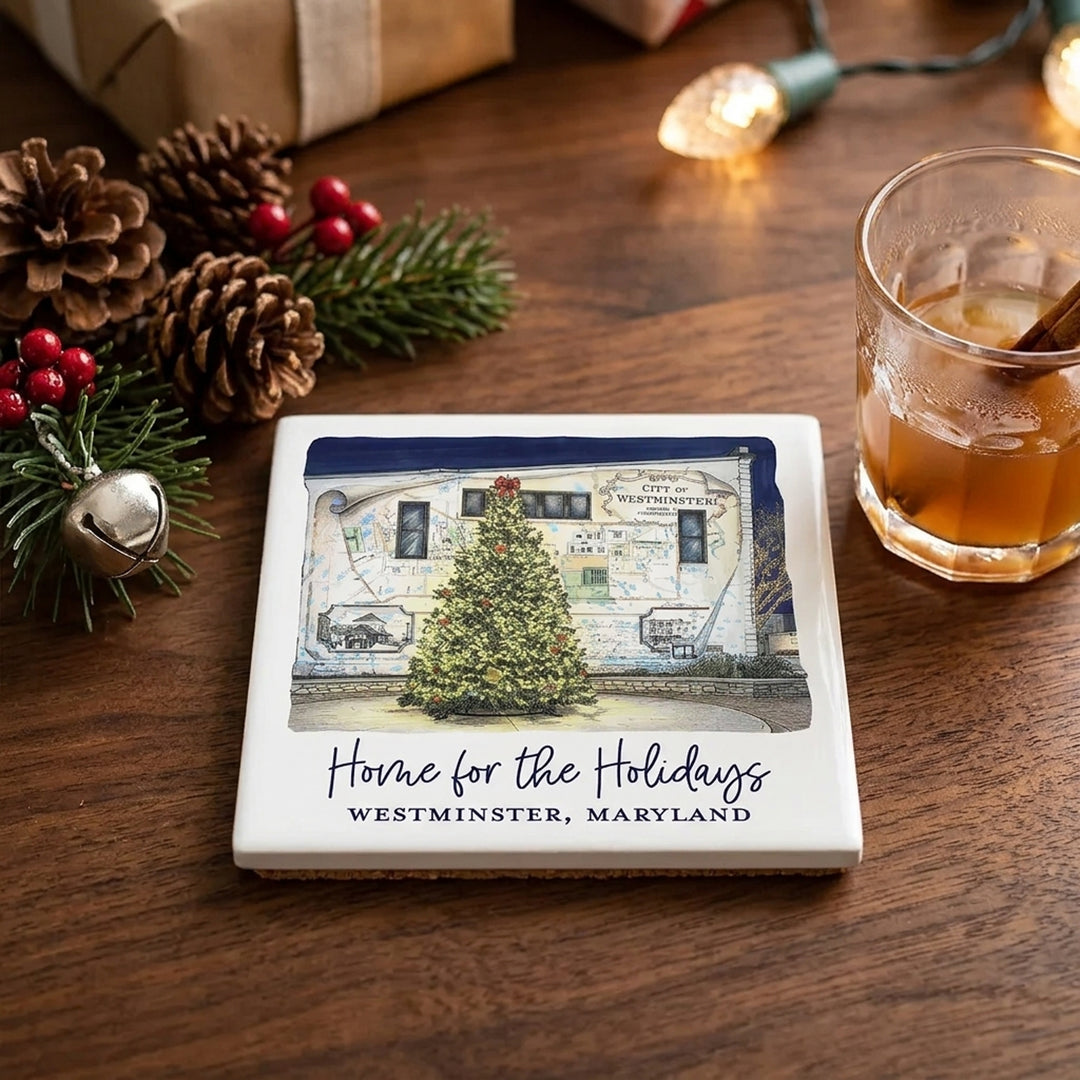 A square ceramic drink coaster featuring a printed illustration of a Christmas tree in front of a building in Westminster, Maryland, with the text &